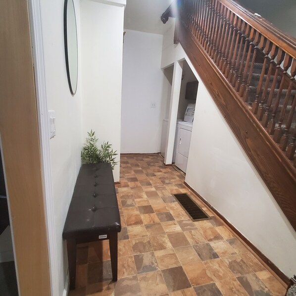 Un pasillo con un banco de madera, una planta en maceta, una lavadora y una escalera.