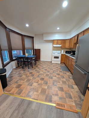 A kitchen with a dining table, wooden cabinets, a refrigerator, and a window with blinds. - The landing on Easterly (Auburn)