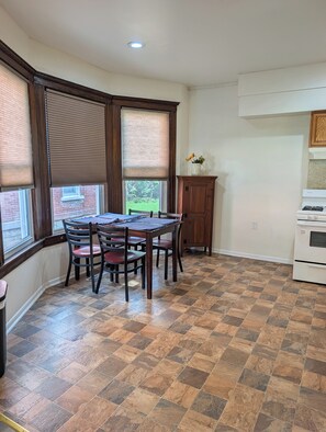 A dining area with a wooden table and chairs, a window with blinds, a cabinet, and a stove.