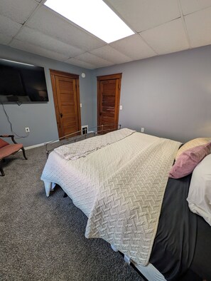 A bedroom with a bed, a television mounted on the wall, and two wooden doors.