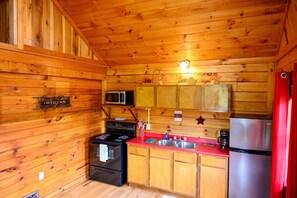 A wooden cabin interior with a kitchen featuring a stove, microwave, cabinets, and a refrigerator.