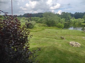 A grassy area with a body of water, trees, and a pile of stones. - Welcome to Fisherman's Dream, located near Hocking (McArthur)