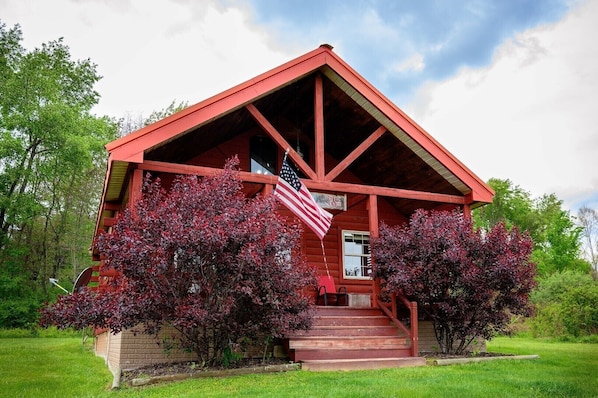 A red wooden cabin with a porch, steps, and an American flag.
