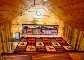 A cozy attic bedroom with a wooden sloped ceiling, a bed with a plaid bedspread, and a headboard with animal-themed pillows.