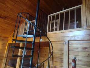A wooden interior with a spiral staircase, a window with bars, and a fire extinguisher.
