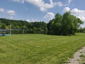 A grassy area with a body of water, trees, and a dock with a boat.