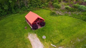 A red cabin with a porch, surrounded by green grass and trees.