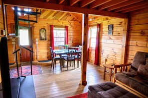 A wooden cabin interior with a dining area, a sofa, and a staircase.