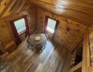 A wooden cabin with a round table and four chairs, two windows with blinds, and a star decoration on the wall.
