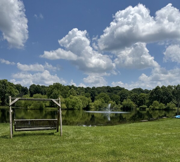 A bench in a grassy area with a lake and trees in the background.