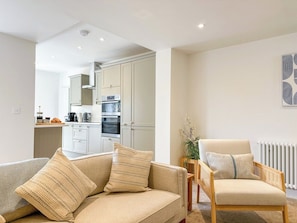 A modern living room with a sofa and armchair, a kitchen in the background, and a radiator on the wall. - Stylish Canterbury Home • Pet-Friendly, Free Parking (Canterbury)