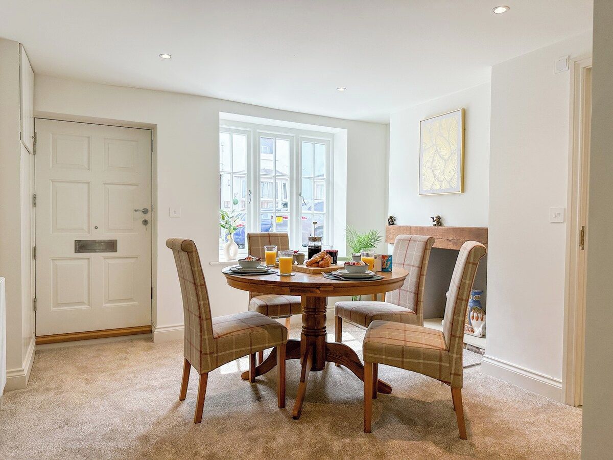 A dining area with a round table, four chairs, and a window with a view of the street.