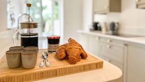 Een keukentafel met een koffiezetapparaat, vier mokken, twee croissants en een pot jam.