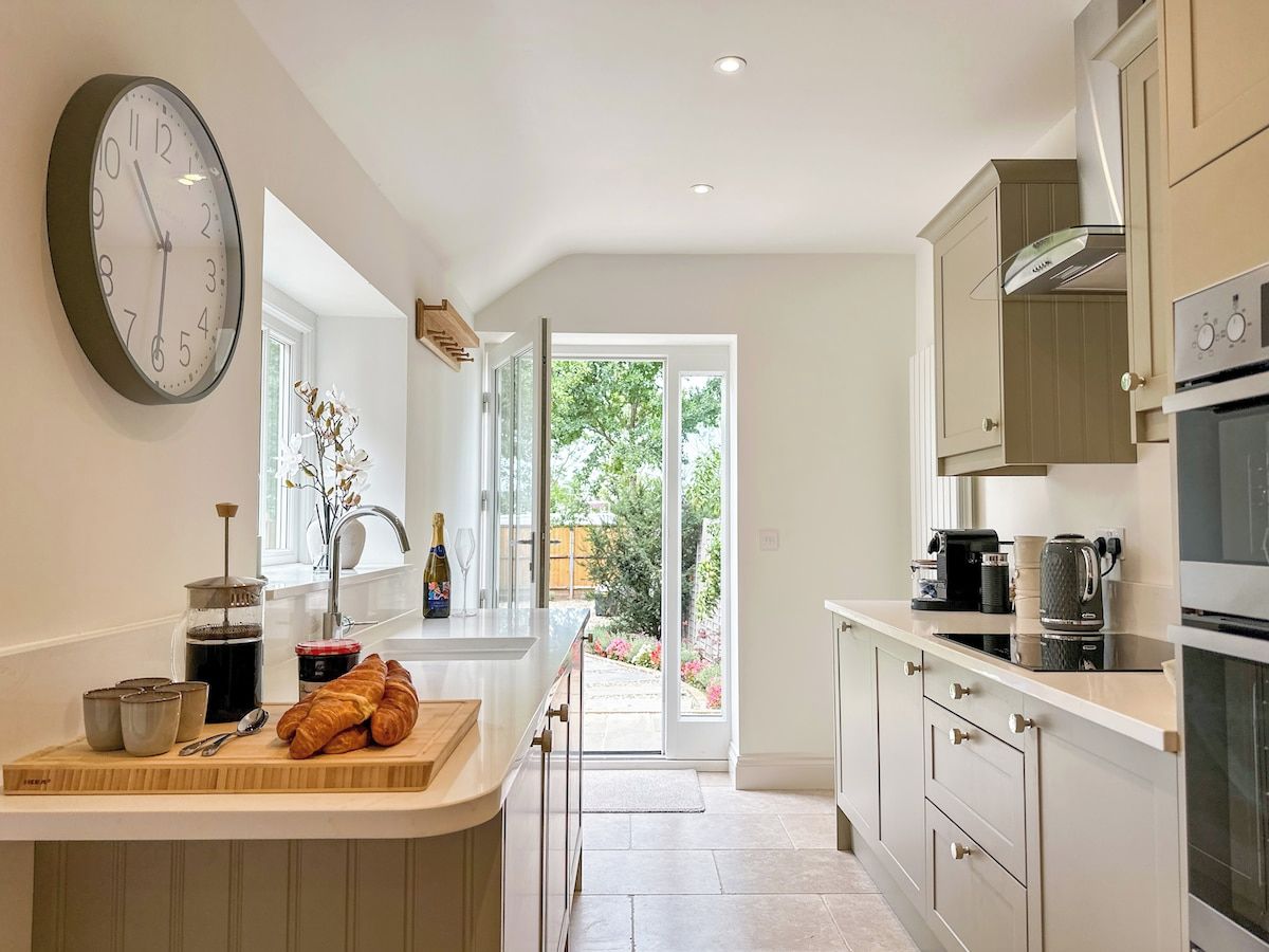 A modern kitchen with a large clock, a coffee machine, and a view to the outside.