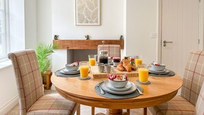 Een eetgedeelte met een ronde houten tafel, gedekt voor het ontbijt, met croissants, sinaasappelsap en een koffiezetapparaat.
