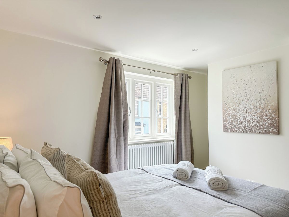 Une chambre à coucher avec un lit, une fenêtre avec des rideaux, un radiateur et une œuvre d’art accrochée au mur.