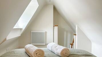 Een slaapkamer met een schuine kap, een radiator en twee opgerolde handdoeken op een bed.