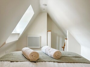 Un dormitorio con techo inclinado, un radiador y dos toallas enrolladas sobre una cama.