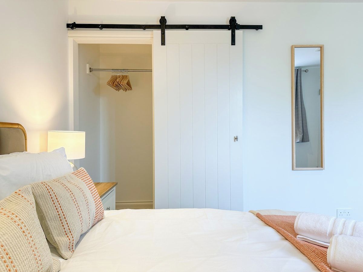 Ein Hotelzimmer mit Bett, Nachttisch, Lampe, Kleiderschrank und Spiegel.