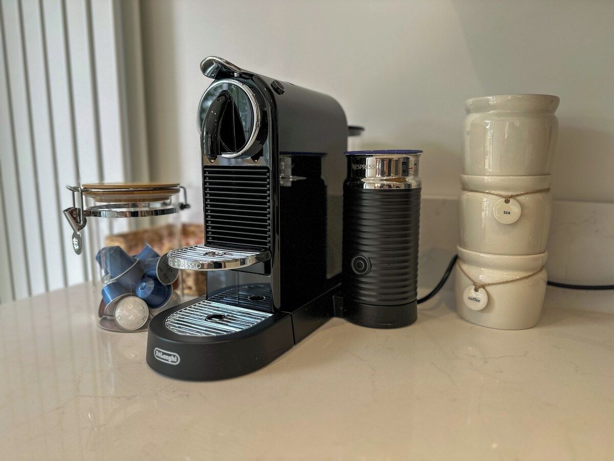 Een koffiezetapparaat met een glazen kan, een Nespresso-capsule en een stapel wegwerpbekers op een aanrecht.