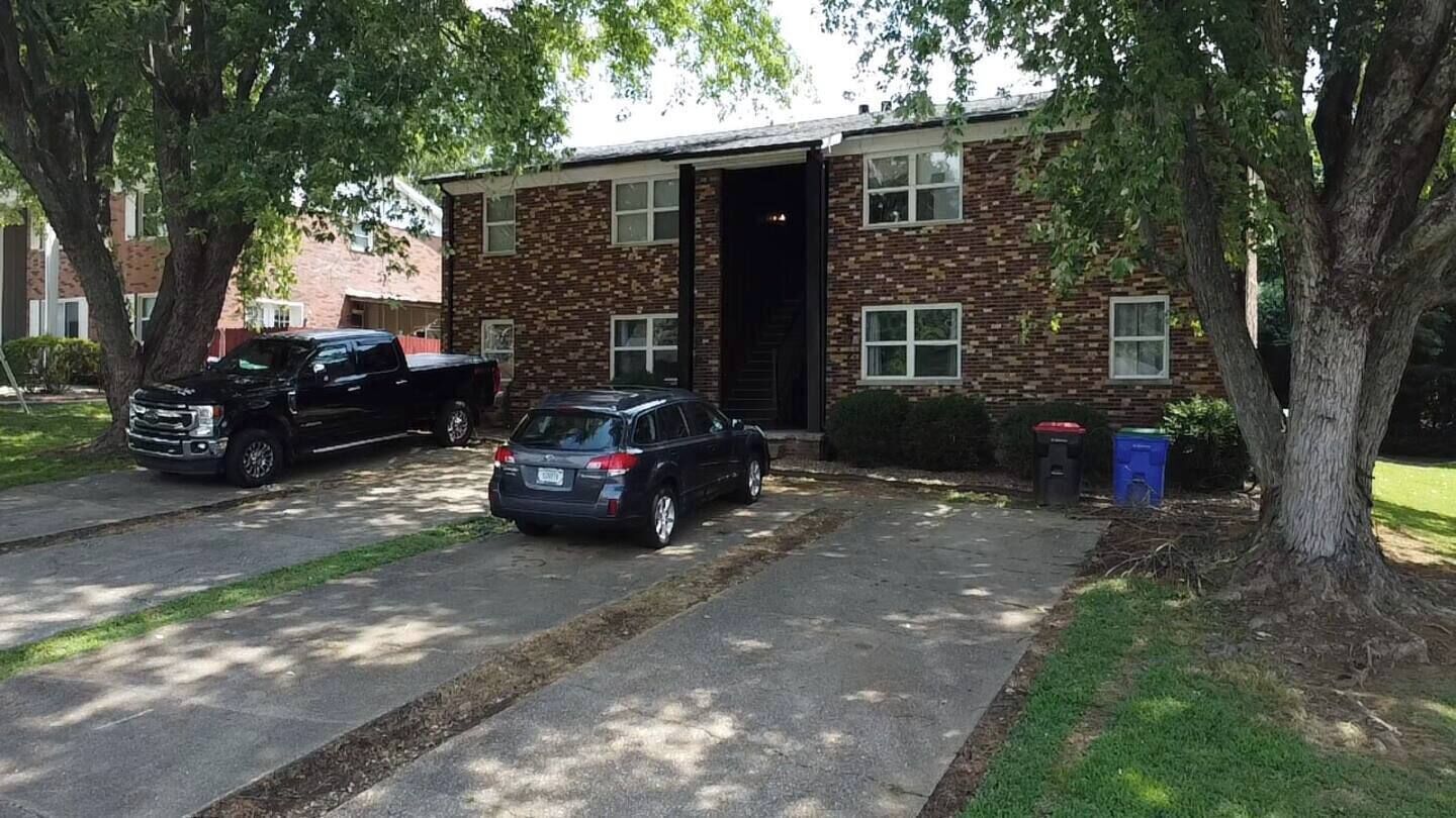 A two-story brick building with a garage door open, parked cars, and trash bins.