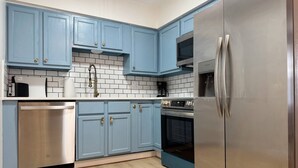 A modern kitchen with blue cabinets, stainless steel appliances, and a tiled backsplash.
