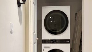 A laundry room with two stacked front-loading washing machines, a white door, and a wall-mounted light fixture.
