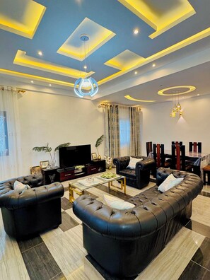A modern living room with a sectional sofa, a flat-screen TV, and a dining area with a table and chairs.
