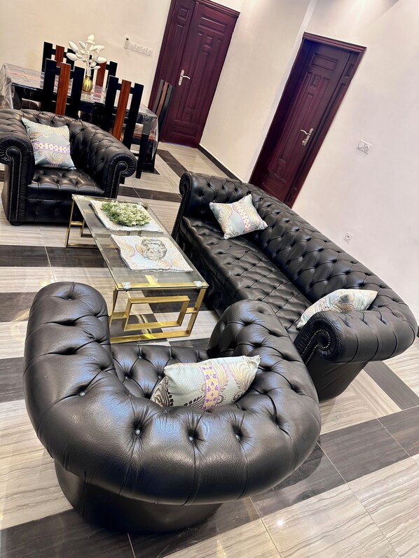 A modern living room with a sectional sofa, a glass coffee table, and a dining area with a wooden table and chairs.