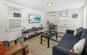 A modern living room with a large TV, a sofa, a coffee table, and a dining area. - A Charming Hidden Gem, two blocks to Moonlight Beach (Encinitas)