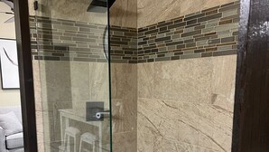 Una ducha con cerramiento de vidrio, suelo de baldosas y un borde decorativo de azulejos.