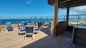 Terraza en la azotea con vistas al océano y al horizonte urbano, con tumbonas y una piscina.