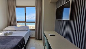 Habitación de hotel con cama, escritorio, televisor y vista a la playa.