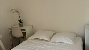 A neatly made bed with white bedding, a small desk with a chair, and a potted orchid on the desk. - Room Notre-Dame de Paris, 20 minutes from Paris SHARED APARTMENT (Épinay-sur-Seine)
