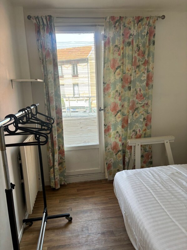 A bedroom with a bed, a radiator, a drying rack, and a window with curtains.