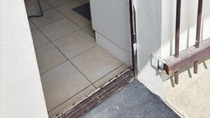 A narrow hallway with a tiled floor leading to a room with a white door and a metal gate. - Room Notre-Dame de Paris, 20 minutes from Paris SHARED APARTMENT (Épinay-sur-Seine)