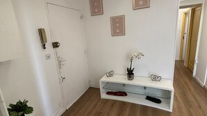 A hallway with a white door, a white console table with a vase and a plant, and a wooden floor. - Room Notre-Dame de Paris, 20 minutes from Paris SHARED APARTMENT (Épinay-sur-Seine)
