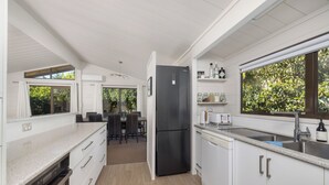 A modern kitchen with white cabinetry, a black refrigerator, and a window overlooking greenery. - Doubtless Bay Vista - Cable Bay Retreat (Cable Bay)