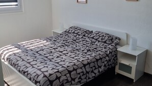 A bedroom with a bed, a bedside table, a nightstand, a hanging light fixture, and framed pictures on the wall. - Cosy 2-bedroom apartment (Givet)