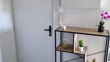 A room with a white door, a black-framed wooden shelf with various items, and a small potted plant.