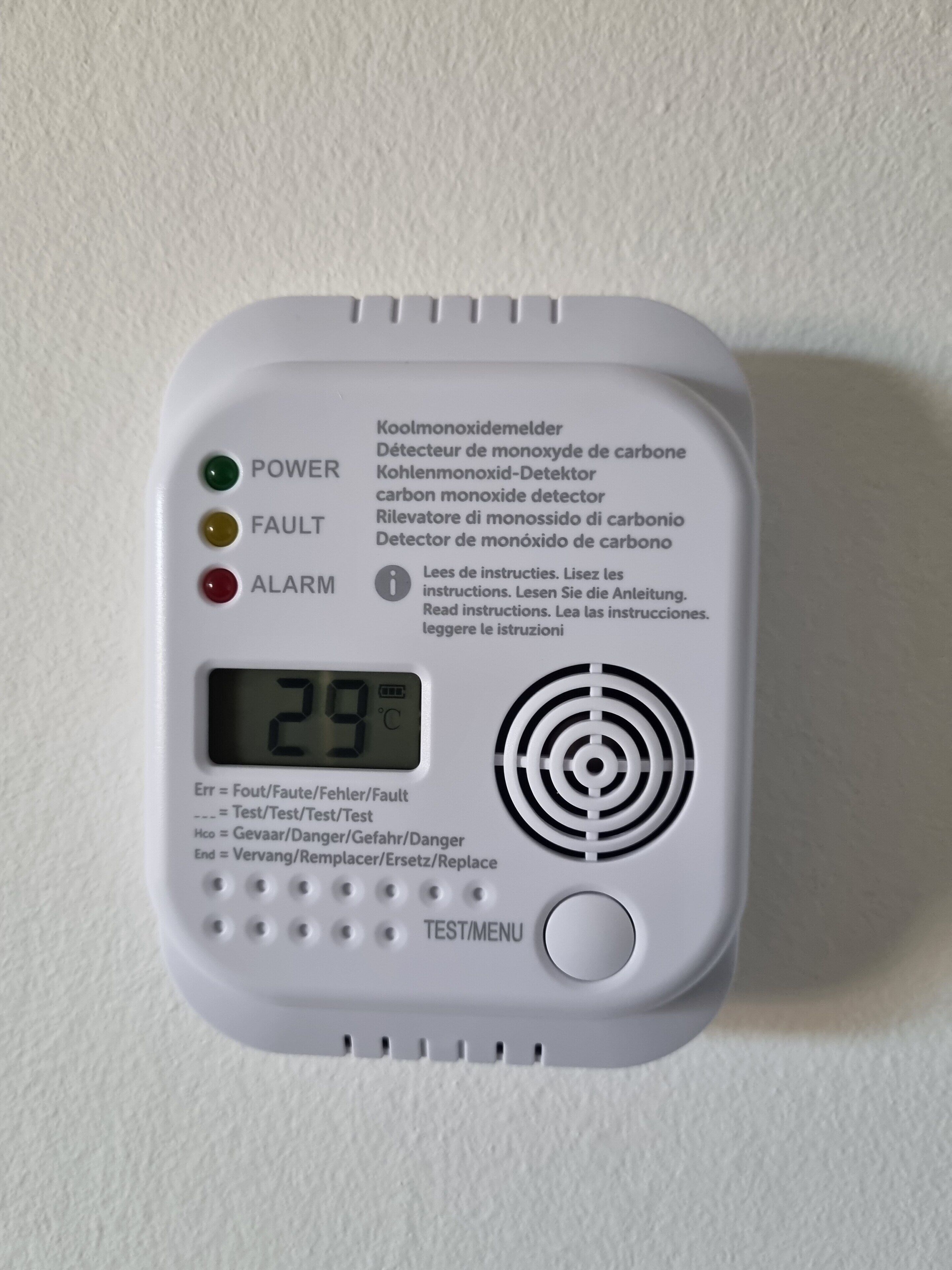 Een wit apparaat met een digitaal scherm, knoppen en meertalige instructies.