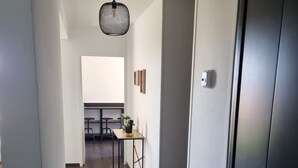 A hallway with a wooden floor, a black door, and a ceiling light fixture. - Cosy 2-bedroom apartment (Givet)