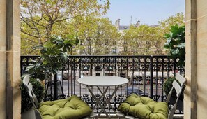 A balcony with a round table and two green cushioned chairs, surrounded by a wrought iron railing. - STEPS AWAY FROM ICONIC LANDMARKS- AN IDEAL CHOICE FOR YOUR NEXT PARISIAN GETAWAY (Paris)
