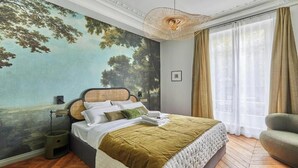 Ein Schlafzimmer mit einer großen Baum-Muralmalerei, einem Bett mit einer grünen Bettdecke, einer Nachttischlampe und einem Fenster mit Vorhängen.