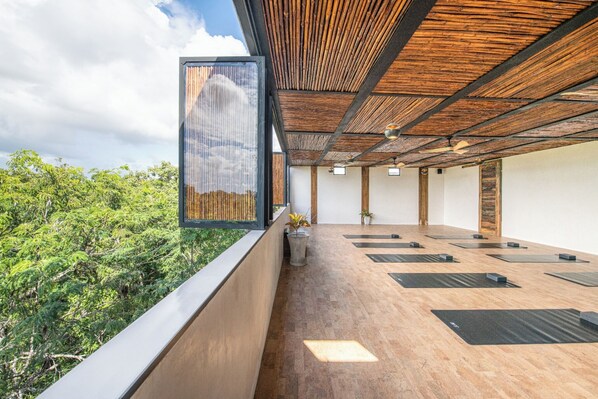 A yoga studio with a wooden floor, black mats, and a view of greenery.