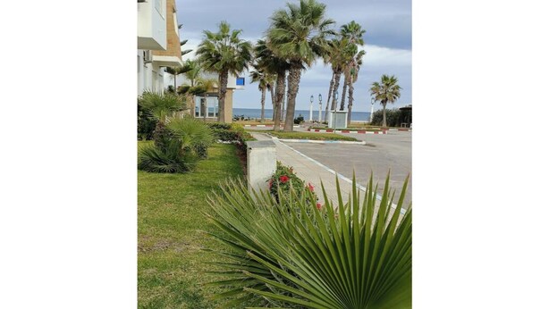 Un hotel con aparcamiento, palmeras y vistas al mar.