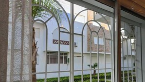 Una ventana con una reja de metal y vista a un edificio de fachada blanca y un pequeño jardín.