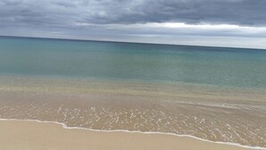 Una playa con agua turquesa cristalina y una orilla arenosa bajo un cielo nublado.