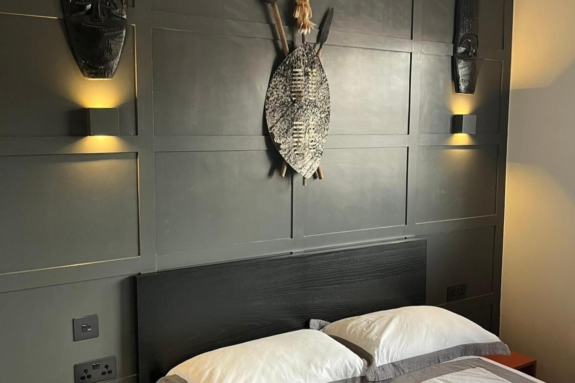 A bedroom with a dark headboard, two bedside lamps, and a decorative fish mounted on the wall.
