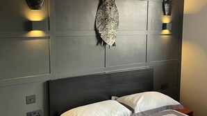 A bedroom with a dark headboard, two bedside lamps, and a decorative fish mounted on the wall.